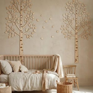 May include: A nursery scene with a wooden crib, a fluffy rug, and a woven basket. Two wooden tree wall decorations and scattered leaf cutouts adorn the wall. The room is decorated in neutral tones, creating a calming and natural atmosphere.