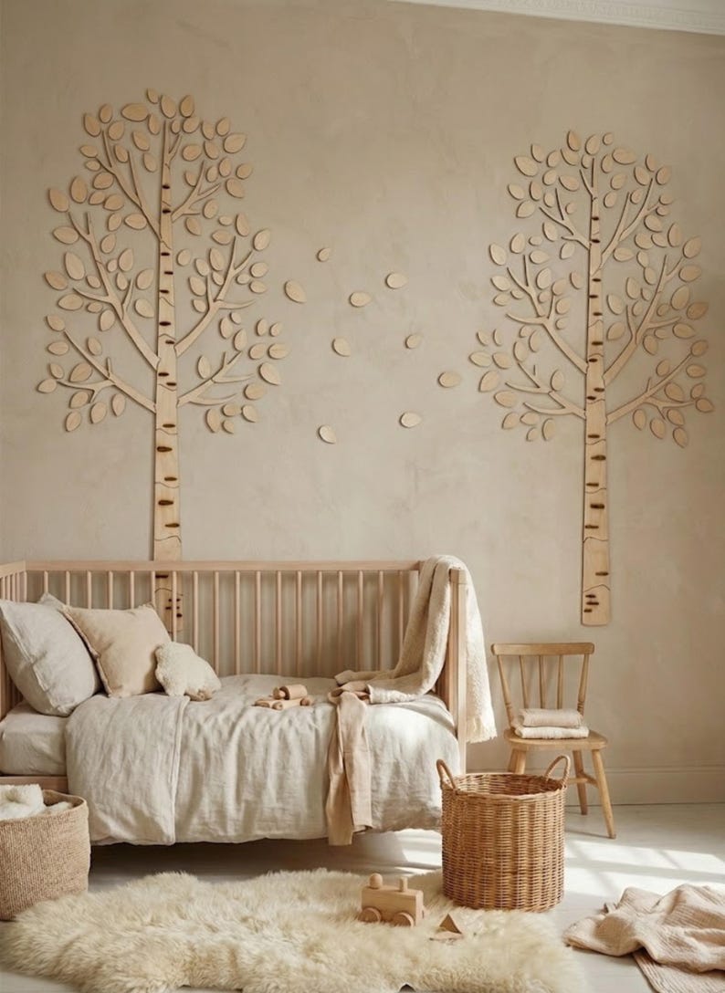 May include: A nursery scene with a wooden crib, a fluffy rug, and a woven basket. Two wooden tree wall decorations and scattered leaf cutouts adorn the wall. The room is decorated in neutral tones, creating a calming and natural atmosphere.