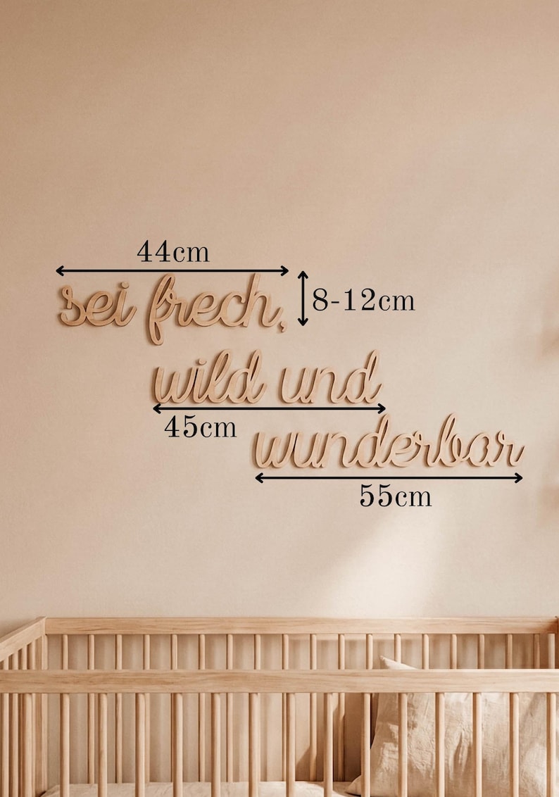 May include: Wooden wall art in a cursive font that reads "sei frech, wild und wunderbar". The top word is 44cm wide, the middle word is 45cm wide, and the bottom word is 55cm wide. The wall art is displayed above a wooden crib.