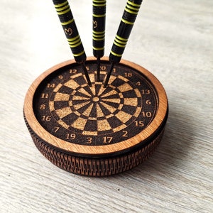 May include: A wooden dartboard with black and white numbers and a cork center. Three black and yellow darts are stuck in the board.