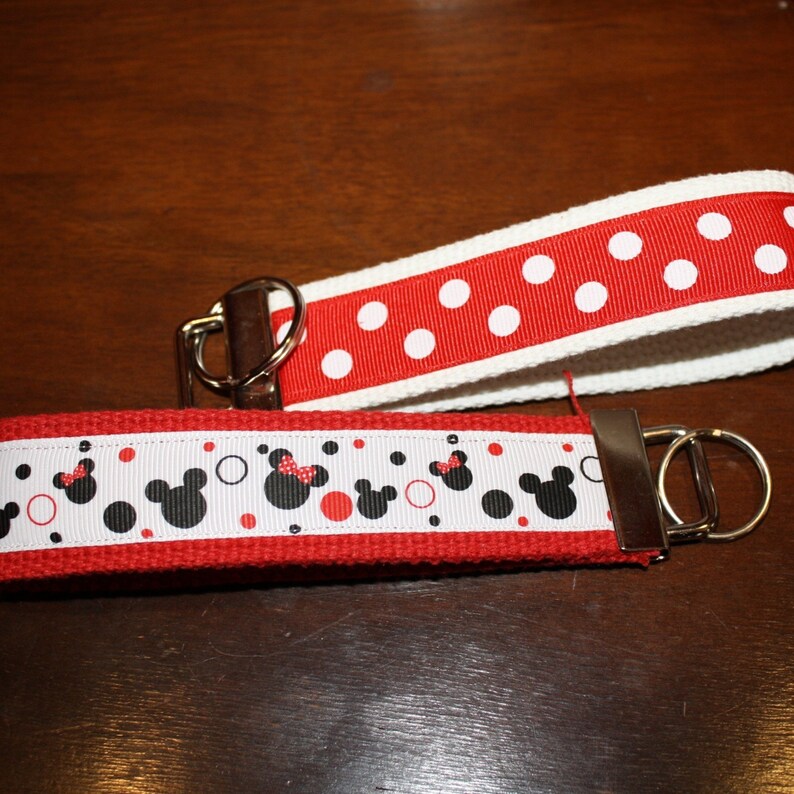 May include: Red and white key chain with a silver key ring. The key chain has a red and white polka dot pattern on one side and a red and white pattern with black Mickey Mouse heads on the other side.