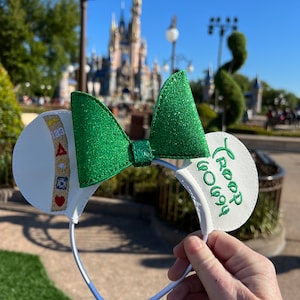 May include: White mouse ears with a green glitter bow and a white embroidered patch that says "Troop 60694".