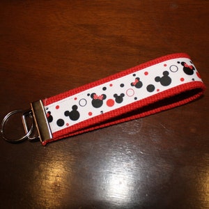 May include: Red and white key chain with a black and white Mickey Mouse pattern. The key chain has a silver key ring.