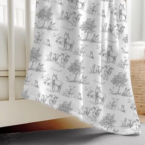 a white blanket with a repeating pattern of farm animals, including cows, horses, and sheep, printed on it.