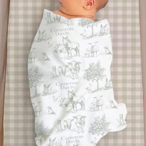 A baby wrapped in a blanket with a repeating pattern of farm animals and trees.