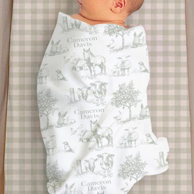 A baby wrapped in a blanket with a repeating pattern of farm animals and trees.