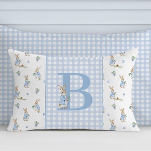 May include: A rectangular pillow with a light blue gingham pattern background. The front pillow has a white center panel with a repeating pattern of rabbits in blue jackets. A large blue letter "B" is centered on the pillow.