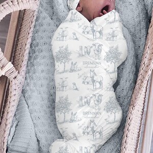 A sleeping baby wrapped in a blanket with a pattern of animals and trees, including a horse and a sheep, is the focus of the image.