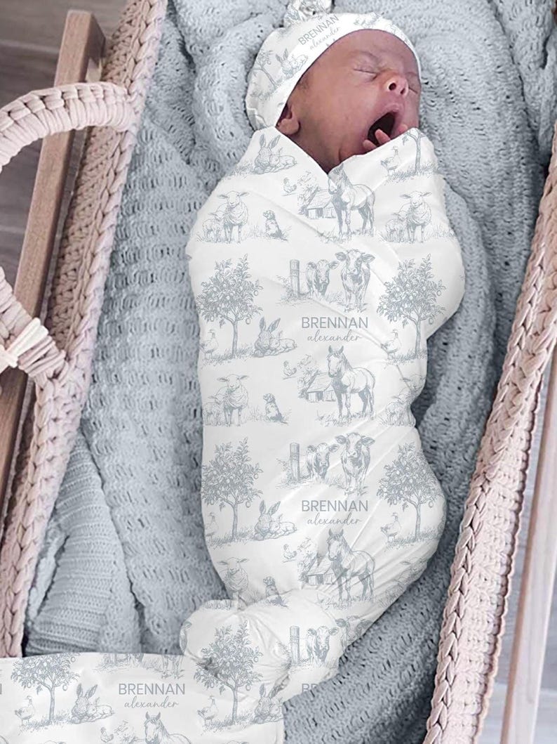 A sleeping baby wrapped in a blanket with a pattern of animals and trees, including a horse and a sheep, is the focus of the image.