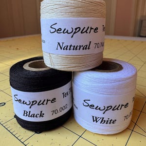 May include: Three spools of Sewpure thread in black, white, and natural colors. Each spool has a label with the Sewpure logo and the color name.