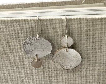 May include: A pair of silver dangle earrings with two oval-shaped ceramic charms. The charms have a white glaze with a distressed finish.