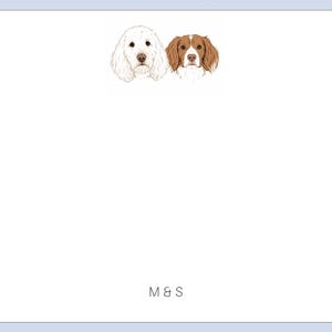May include: A white rectangular stationery card featuring a light blue border. At the top, there are two illustrated dog heads: one white and one brown and white. At the bottom center, the letters M&S are printed in a simple black font.
