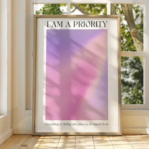 May include: A framed print with a pink and purple gradient background. The text "I AM A PRIORITY" is at the top of the print. The text "Everything is falling into place as it's meant to be" is at the bottom of the print.