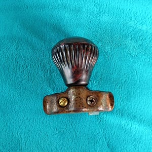 May include: A vintage-style dark brown, fluted, spherical knob attached to a weathered, metallic, horizontal mounting bracket. The bracket features two distinct screws, one brass-colored and one dark, securing the assembly together.
