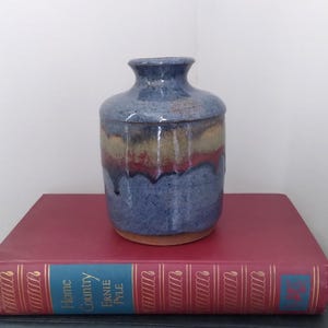 May include: A small, blue ceramic vase with a brown, yellow, and red glaze. The vase has a rounded body and a narrow neck.
