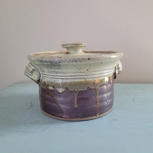 May include: A ceramic casserole dish with a lid. The dish is glazed in shades of brown, purple, and white. The lid has a knob on top.