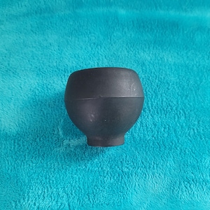 May include: A black rubber plunger with a rounded top and a narrow base. The plunger is set against a turquoise background.