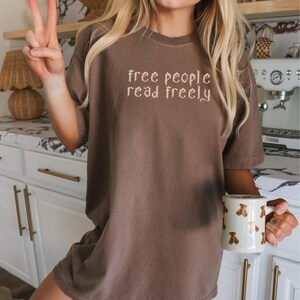May include: An oversized brown t-shirt with the text "free people read freely" in a light pink colour.