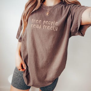 May include: An oversized brown t-shirt with the text "free people read freely" printed on the front.