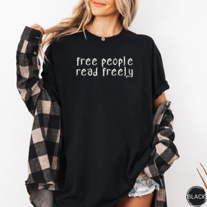 May include: Black long-sleeve t-shirt with the text "free people read freely" in a gothic font. The shirt is worn with a black and tan plaid shirt. A small black tag is visible on the bottom right.