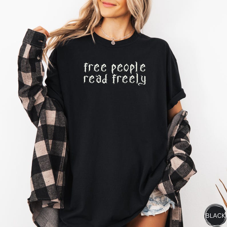 May include: Black long-sleeve t-shirt with the text "free people read freely" in a gothic font. The shirt is worn with a black and tan plaid shirt. A small black tag is visible on the bottom right.