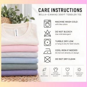 Puede incluir: Una pila de camisetas para ni&ntilde;os peque&ntilde;os Bella+Canvas 3001T dobladas en crema, rosa, gris, azul, verde y morado. La imagen incluye instrucciones de cuidado: lavar a m&aacute;quina en fr&iacute;o, no usar lej&iacute;a, secar en secadora a baja temperatura.