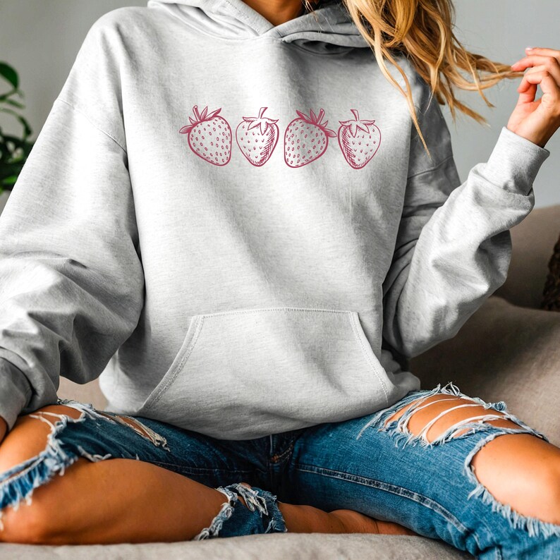 May include: A gray hoodie with a pink strawberry graphic print. The hoodie has a drawstring hood and a kangaroo pocket.