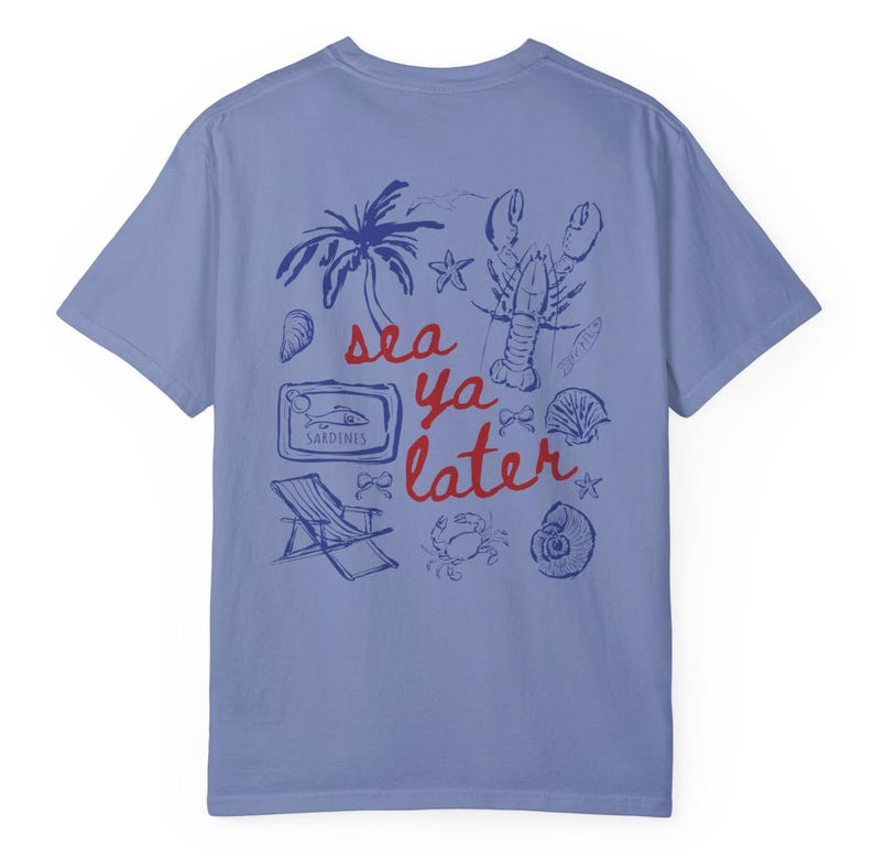 Puede incluir: Una camiseta azul claro con un estampado gr&aacute;fico azul y rojo de una langosta, una palmera, conchas marinas y una lata de sardinas. El texto de la camiseta dice "sea ya later".