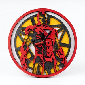 以下が含まれることがあります： アイアンマンのシルエットが描かれた赤と黒の木製壁掛け時計。時計は黄色と黒の背景に円形のデザインが施されています。