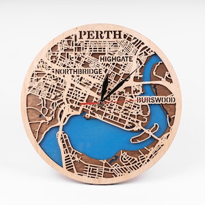 Puede incluir: Un reloj de madera con un mapa de Perth, Australia, en la cara. Las manecillas del reloj son negras y rojas, y el mapa está delineado en marrón. Los nombres de las ciudades "Northbridge", "Highgate" y "Burswood" son visibles en el mapa.