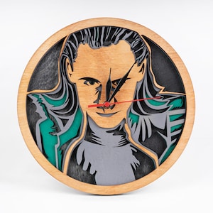 以下が含まれることがあります： 人気映画のキャラクターをレーザーカットしたデザインのウッドクロック。時計の文字盤は黒で、赤と黒の時計針が付いています。キャラクターの顔は緑とグレーの背景で確認できます。