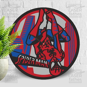 May include: A black and red round wall clock with a Spiderman graphic. The clock features a red and blue Spiderman hanging upside down between two buildings. The text "SPIDERMAN" is written in white letters on the clock face.