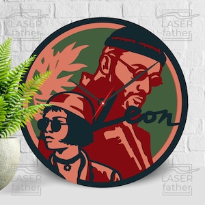 Può includere: Un orologio rotondo in legno con un design rosso, verde e nero che presenta un'immagine stilizzata di Leon e Mathilda dal film Leon: The Professional. Il quadrante dell'orologio è nero con lancette bianche e la parola "Leon" è scritta in un font stilizzato.
