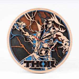 May include: A wooden wall clock featuring a laser-cut design of Thor, the Norse god of thunder, holding his hammer. The clock face is surrounded by a blue and black lightning bolt design. The word "THOR" is printed in black letters below the image.
