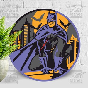 Peut inclure: Une horloge ronde de Batman en violet et noir sur fond jaune. L'horloge représente une silhouette de Batman debout sur un bâtiment avec une ville en arrière-plan. L'horloge est ronde et possède un cadran noir avec des aiguilles argentées.