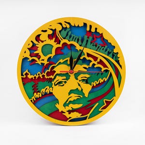May include: A yellow, green, blue and red wooden clock with a cutout of Jimi Hendrix's face and the text "Jimi Hendrix".