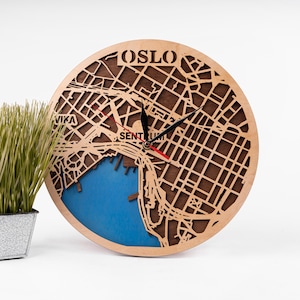 May include: A wooden clock with a map of Oslo, Norway, on the face. The clock has a blue background and black hands. The text "OSLO" is printed on the top of the clock.