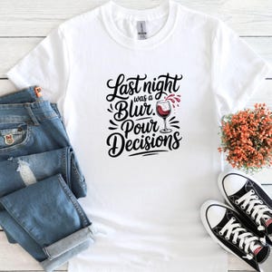 May include: White t-shirt with a black graphic that says "Last night was a blur. Pour decisions." with a glass of red wine pouring out of it.