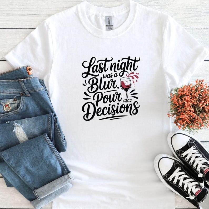 May include: White t-shirt with a black graphic that says "Last night was a blur. Pour decisions." with a glass of red wine pouring out of it.