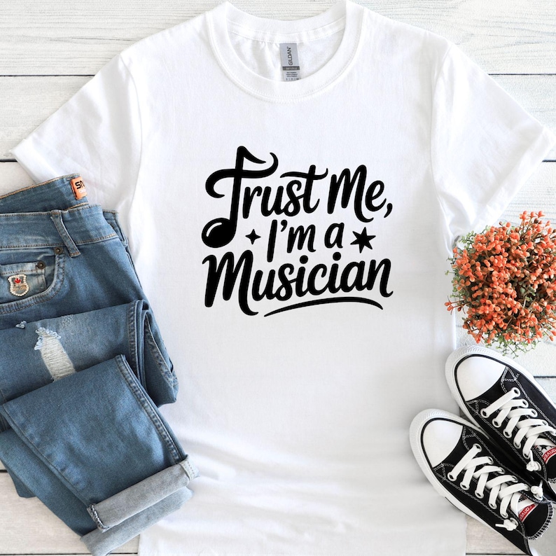 May include: White t-shirt with the text "Trust Me, I'm a Musician" in a black, cursive font. The shirt is paired with blue jeans and black and white sneakers. A small bouquet of orange flowers is also present.