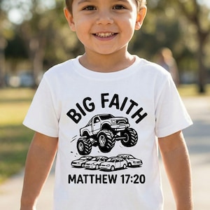 May include: White t-shirt featuring a black graphic of a monster truck jumping over several cars. The words "BIG FAITH" are above the truck, and "MATTHEW 17:20" is printed below.