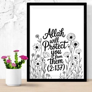 May include: Black framed art print with the text "Allah will protect you from them (2:137)" in a cursive font, surrounded by black and white floral illustrations. A small white vase with pink flowers sits to the left.