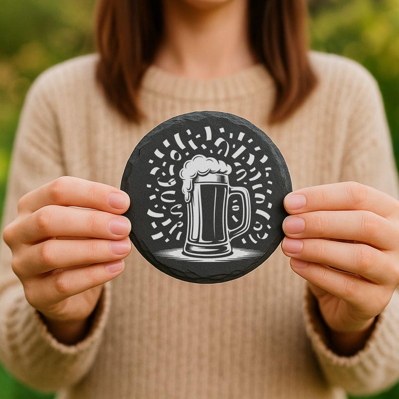 May include: A round, black slate coaster featuring a white illustration of a beer mug with foam and celebratory confetti. The coaster is held by a person wearing a beige sweater, with a blurred green background.