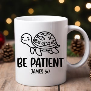 May include: White ceramic mug featuring a black and white cartoon turtle with fish on its shell. The mug has the text "BE PATIENT" and "JAMES 5:7" printed in black.