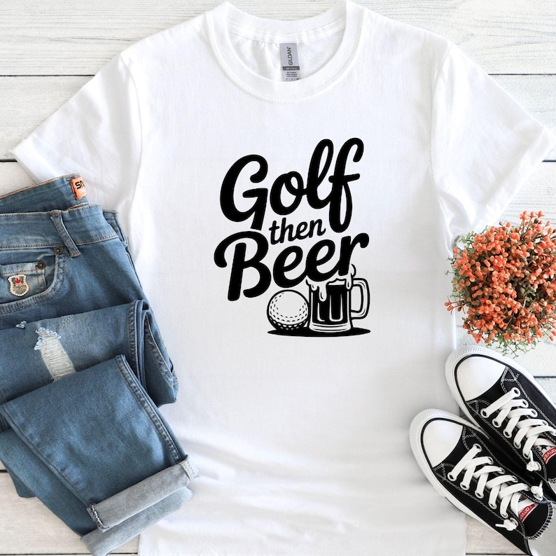 May include: White t-shirt with the text "Golf then Beer" in a black, bold font. A golf ball and beer mug graphic are below the text. The shirt is paired with blue jeans and black and white sneakers.