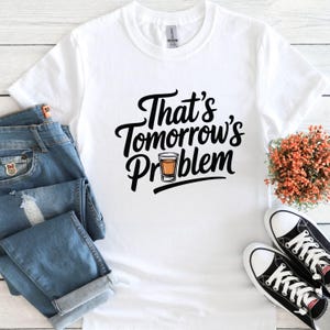 May include: White t-shirt with black text that reads "That's Tomorrow's Problem" and a small image of a shot glass with a yellow liquid.