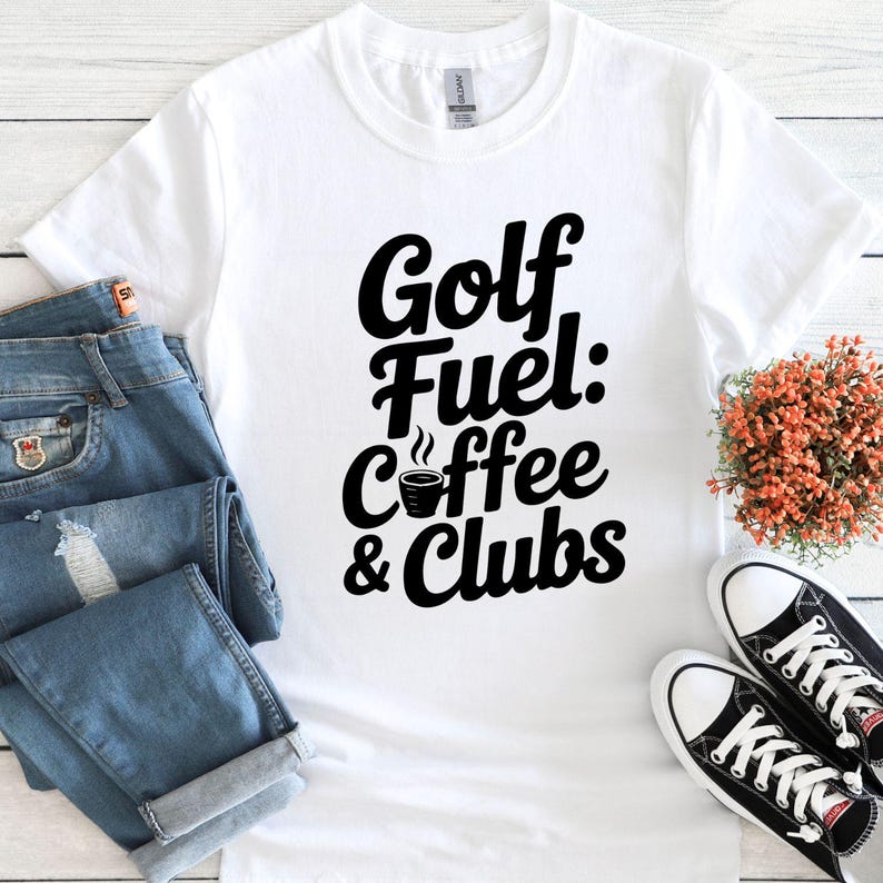 May include: White t-shirt with the text "Golf Fuel: Coffee & Clubs" in black. The shirt is paired with blue jeans and black and white sneakers. A small bouquet of orange flowers is also present.