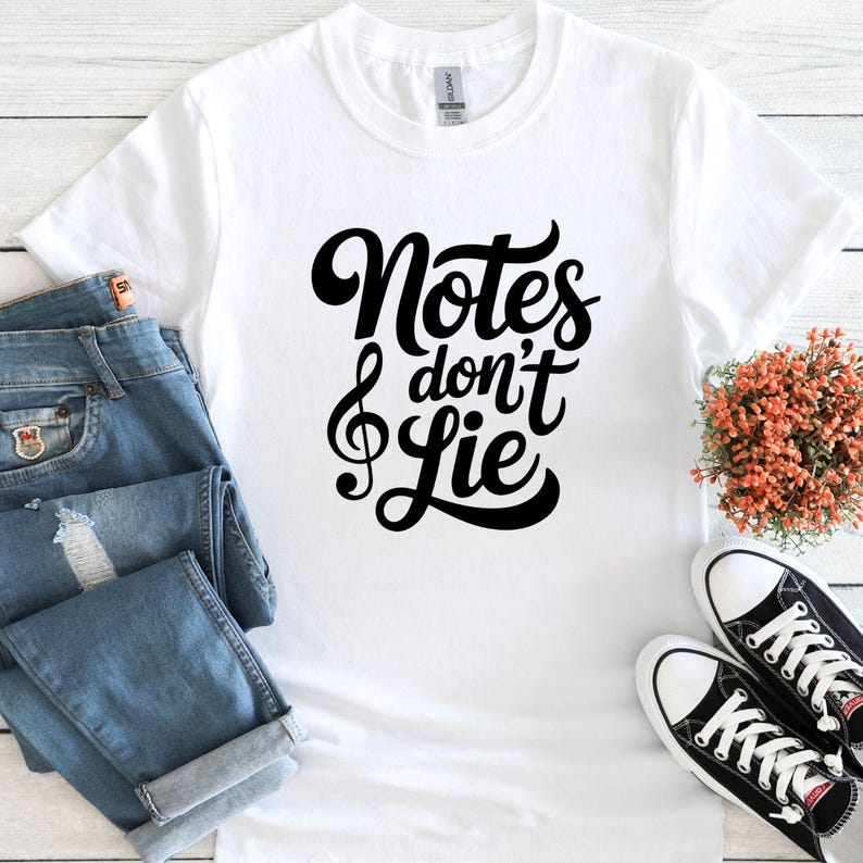 May include: White t-shirt with the text "Notes don't Lie" in black script, featuring a treble clef. The shirt is paired with blue jeans and black and white sneakers, suggesting a music-themed style.