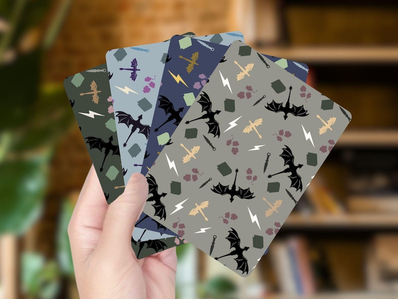 Op de afbeelding: Een hand die een stapel kaarten met patronen vasthoudt. Elke kaart heeft een herhalend ontwerp van zwarte draken, bliksemschichten, zwaarden en andere fantasie-elementen in verschillende kleuren, waaronder grijs, blauw en groen.
