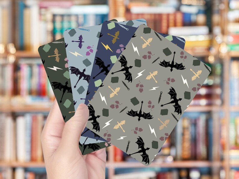 Op de afbeelding: Een hand die vier kaarten met patronen vasthoudt. Elke kaart heeft een herhalend patroon van zwarte draken, bliksemschichten en andere fantasie-elementen in tinten groen, blauw en grijs. De achtergrond is een vage boekenkast.